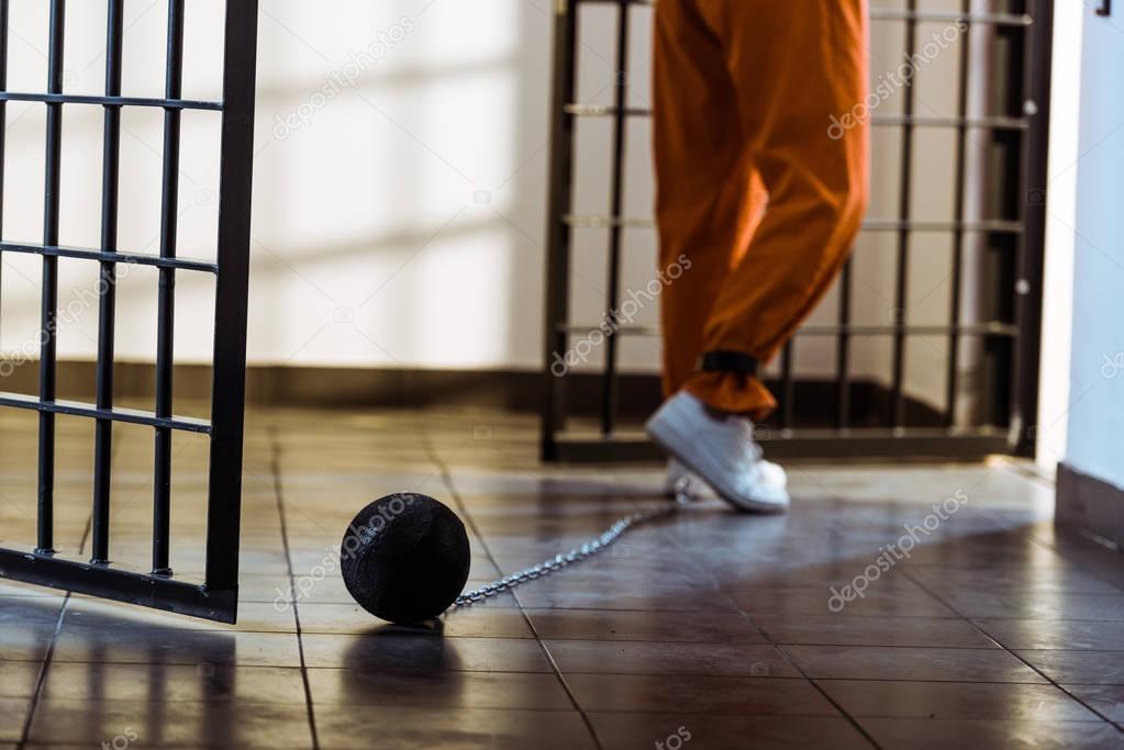 cropped image of prisoner walking in orange uniform with weight tethered to leg