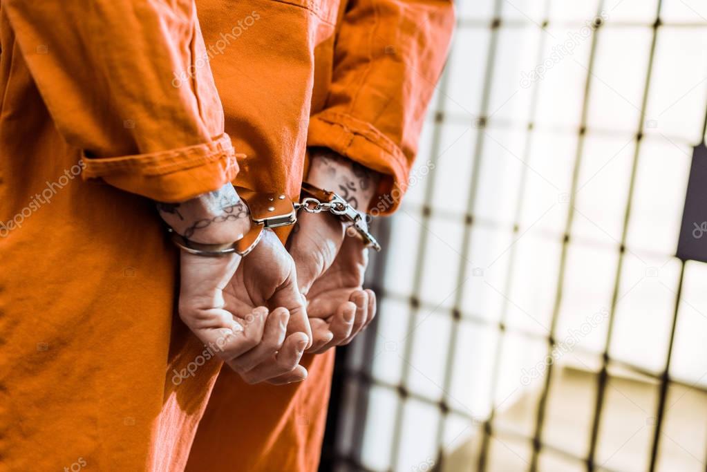 cropped image of tattooed prisoner standing in handcuffs in corridor