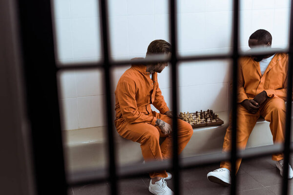 multiethnic prisoners playing chess behind prison bars