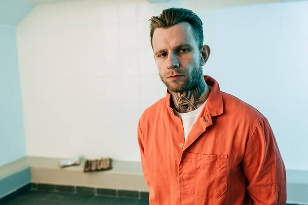 tattooed prisoner looking at camera in prison cell