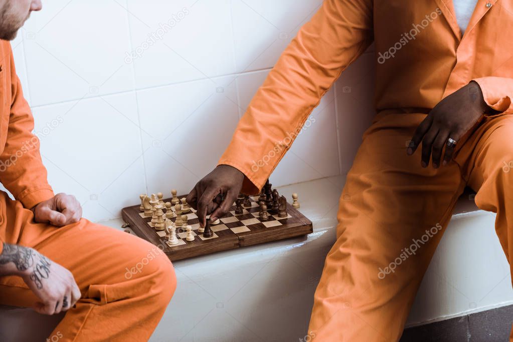 cropped image of multicultural prisoners playing chess in prison cell