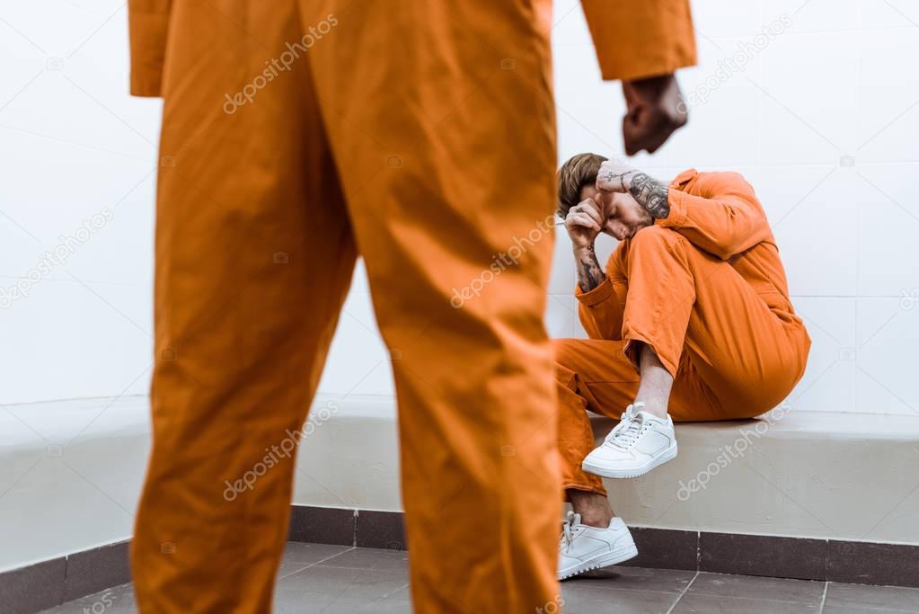 cropped image of african american prisoner standing with fist, other prisoner covering face 