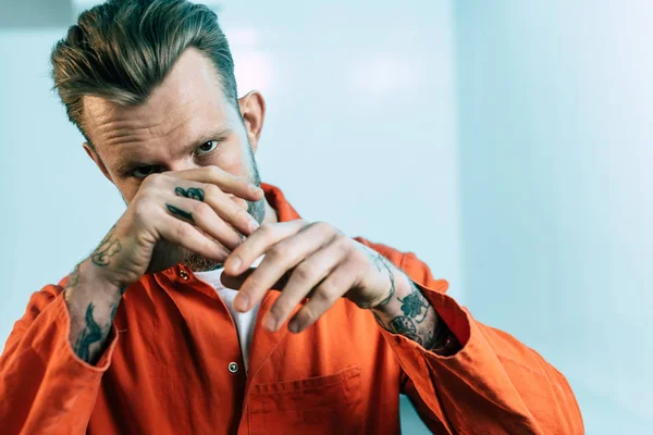 Prisioneiro Com Tatuagens Cobrindo Rosto Com Mãos Olhando Para Câmera — Fotografia de Stock