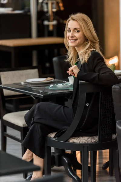 Красивая Улыбающаяся Женщина Смотрит Камеру Сидя Столом Кафе — Бесплатное стоковое фото