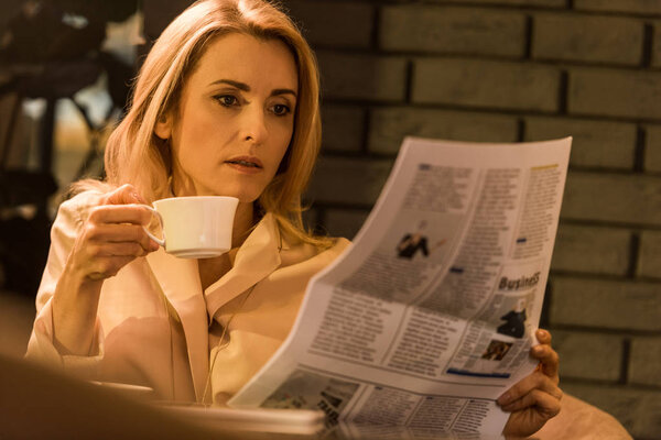 portrait of focused businesswoman with cup of coffee reading newspaper in cafe