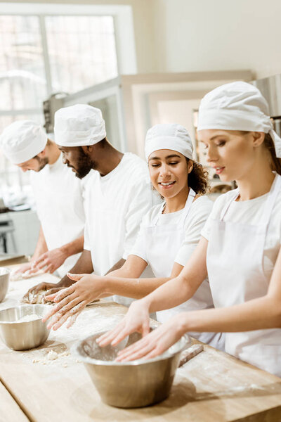 group of young multiethnic baking manufacture workers kneading dough together