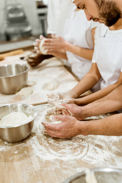 cropped shot of group of baking manufacture workers kneading dough together