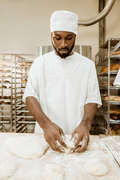handsome african american baker preparing raw dough for pastry on baking manufacture