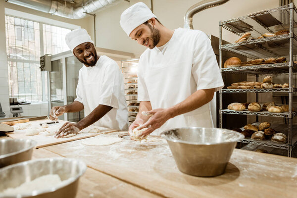 happy bakers kneading dough together at baking manufacture and talking