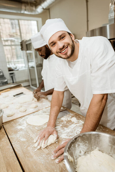 happy handsome bakers kneading dough together at baking manufacture