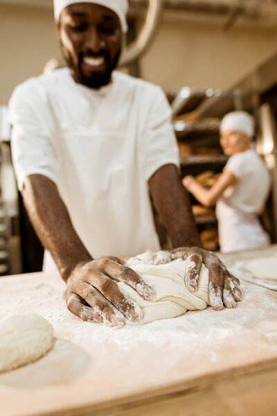 close-up shot of african american baker kneading dough at baking manufacture