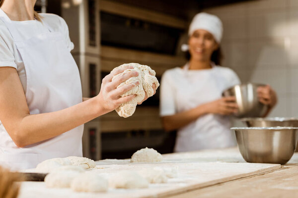 cropped shot of female baker kneading dough at baking manufacture