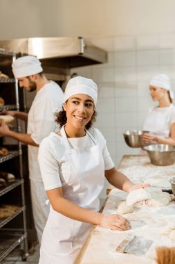 mutlu kadın baker arka plan üzerinde bulanık üretim çalışma meslektaşları süre pişirme, hamur yoğurma