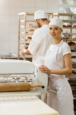 female baker with industrial dough roller at baking manufacture clipart