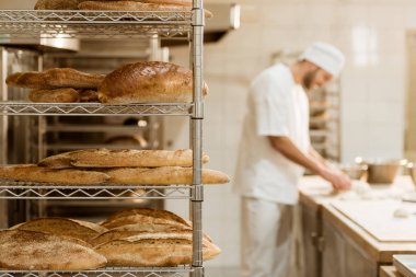 shelves with fresh bread and blurred baker on background at baking manufacture clipart