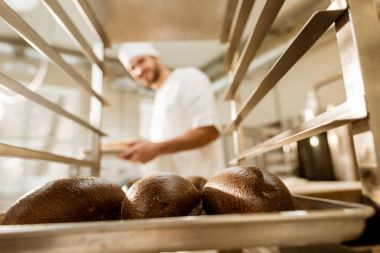 happy baker looking at fresh loaves of bread on baking manufacture clipart