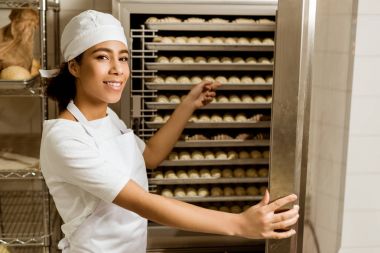 Bayan baker hamur üretim pişirme, endüstriyel fırın içinde gösteren gülümseyen