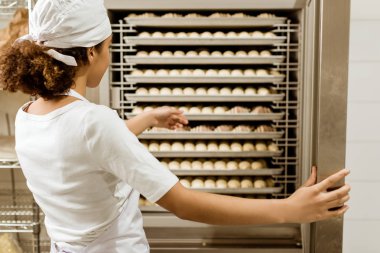 female baker pointing at dough inside of industrial oven at baking manufacture clipart