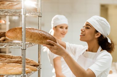 üretim sırasında arka plan üzerinde bulanık duran onun meslektaşım pişirme, raflarda taze ekmek somunları koyarak kadın baker