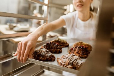 Bayan baker üretim pişirme üzerinde taze pişmiş kruvasanlar tepsi tutarak kırpılmış atış