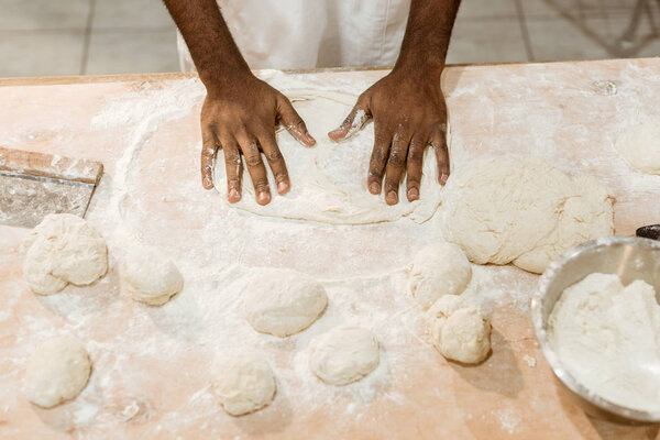 cropped shot of african american baker kneading dough for pastry on messy table