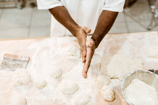 cropped shot of african american baker preparing dough balls for pastry and covering hands in flour