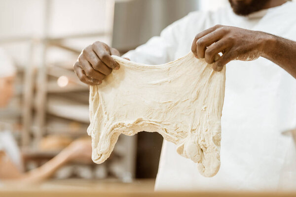 cropped shot of african american baker preparing dough on baking manufacture