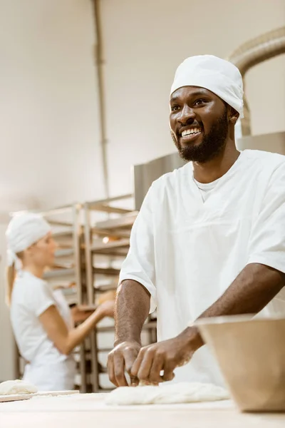 Fröhlicher Afrikanisch Amerikanischer Bäcker Knetet Teig Während Seine Kollegin Backbereich — Stockfoto