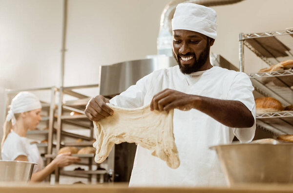 happy handsome african american baker preparing dough on baking manufacture