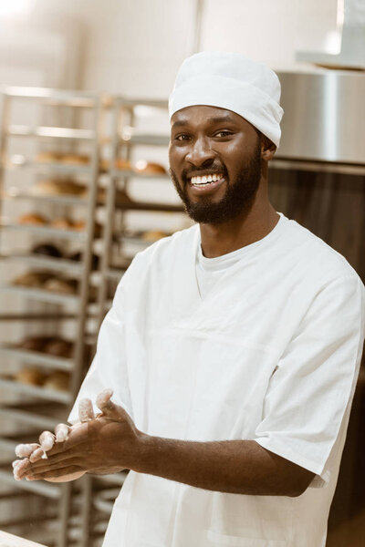 handsome african american baker with flour on hands at baking manufacture