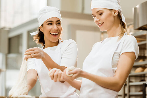 happy female bakers kneading dough together at baking manufacture