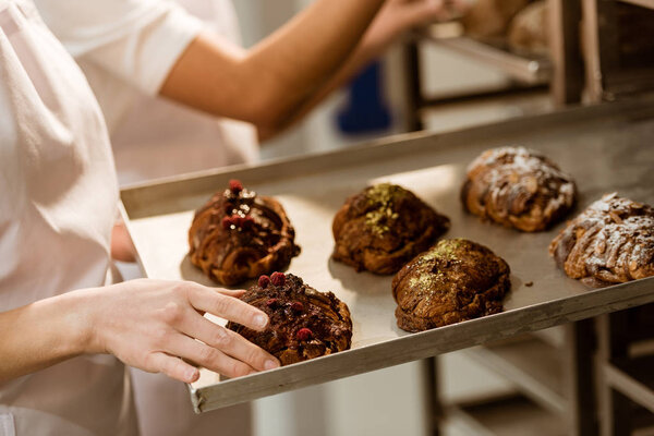 cropped shot of female baker taking out tray with sweet pastry from oven