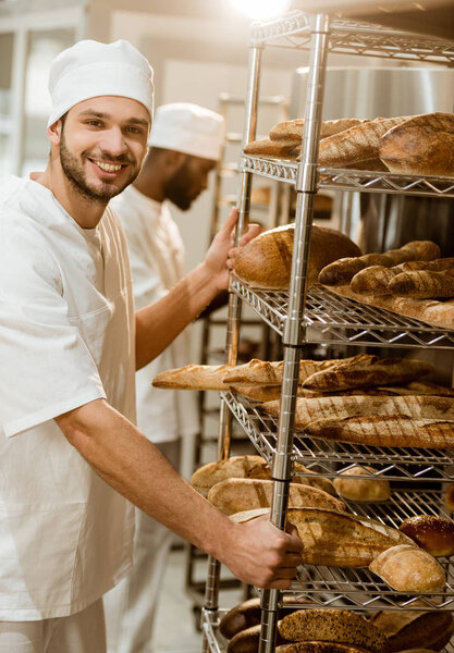 baker near shelves with fresh bread loaves at baking manufacture