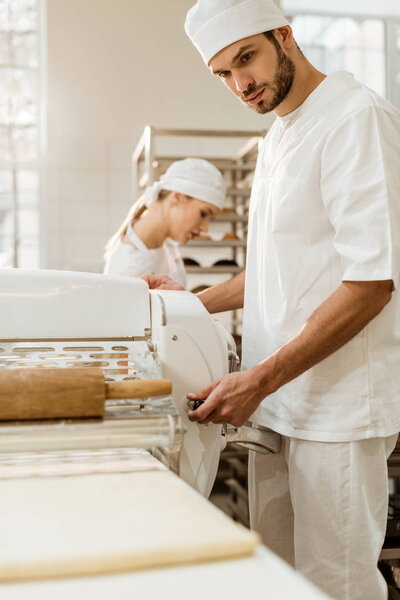 handsome baker working with industrial dough roller at baking manufacture