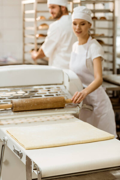 female baker using industrial dough roller at baking manufacture