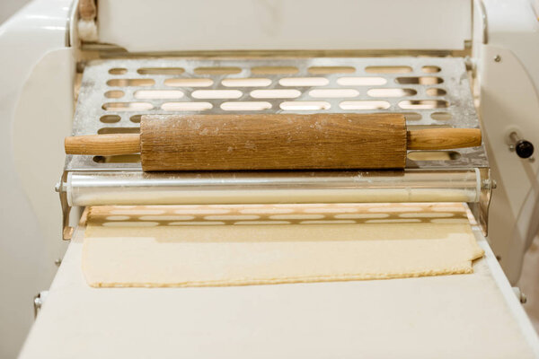 Close-up shot of industrial dough roller with traditional rolling pin