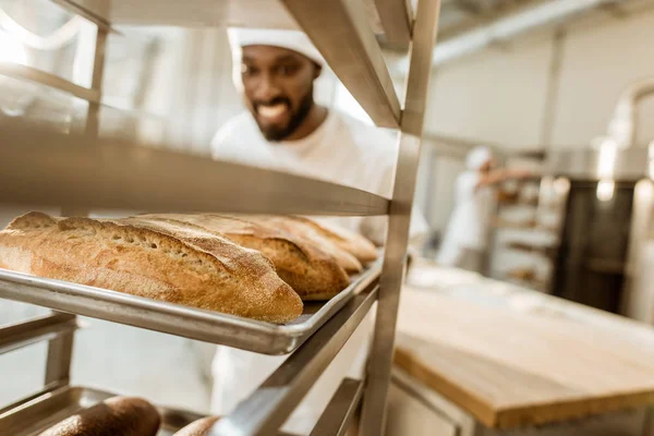 Szczęśliwy African American Baker Patrząc Świeże Bochenków Chleba Pieczenia Produkcji — Zdjęcie stockowe