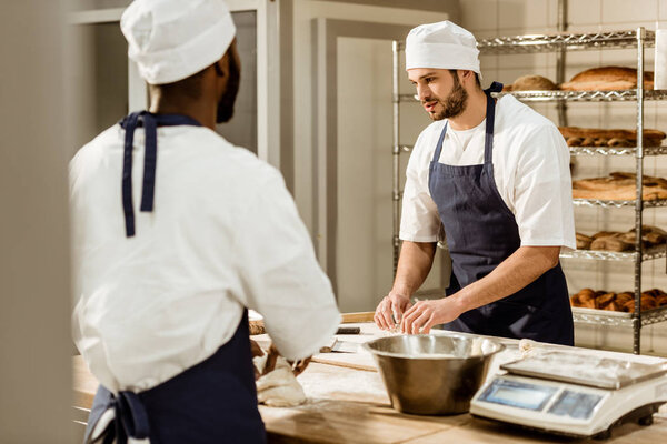 bakers kneading dough together at baking manufacture and chatting