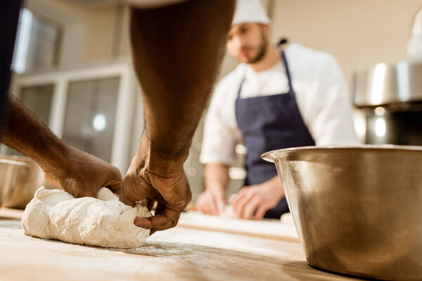 cropped shot of bakers kneading dough together at baking manufacture