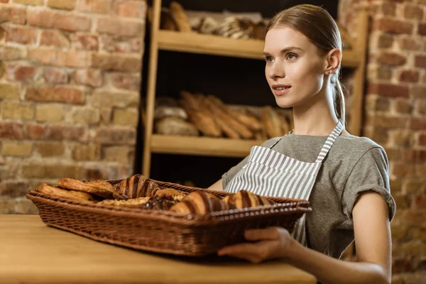 beautiful young baker with basket of croissants at pastry store