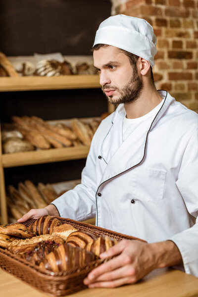 handsome baker holding tray with croissants at pastry store