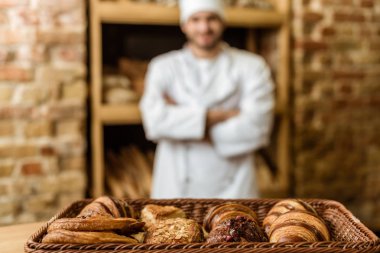 çapraz kolları kruvasan ön plan üzerinde sepet ile pasta dükkanındaki ayakta olan bulanık baker