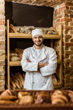pasta dükkanda duran çapraz kollu yakışıklı gülümseyen baker
