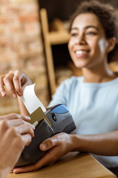 close-up shot of cashier with pos terminal receiving purchase from client at pastry store