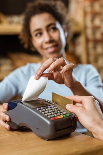 cropped shot of cashier with pos terminal receiving purchase from client at pastry store