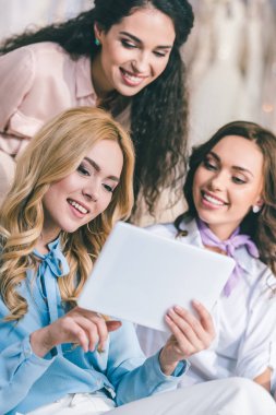 Gelin ve nedime elbiseler seçme ve tablet düğün moda dükkanda bakarak gülümseyen genç