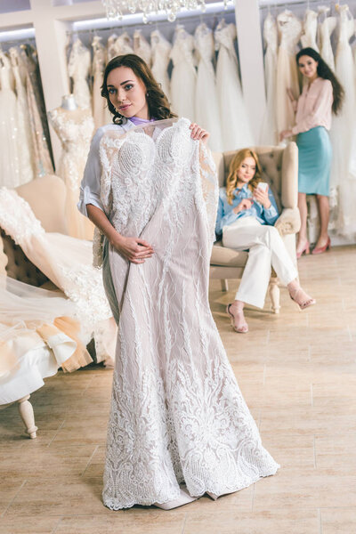 Привлекательная женщина в свадебных платьях и подружка невесты в свадебном салоне
