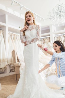 Blonde bride in lace dress and tailor during dress fitting in wedding salon