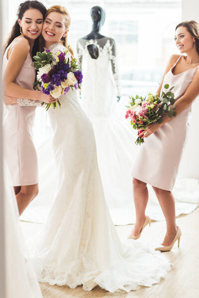 Smiling women in wedding dresses embracing in wedding fashion shop