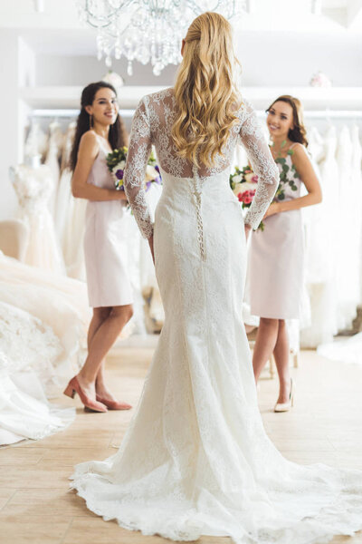 Attractive bride and bridesmaids with flowers in wedding atelier